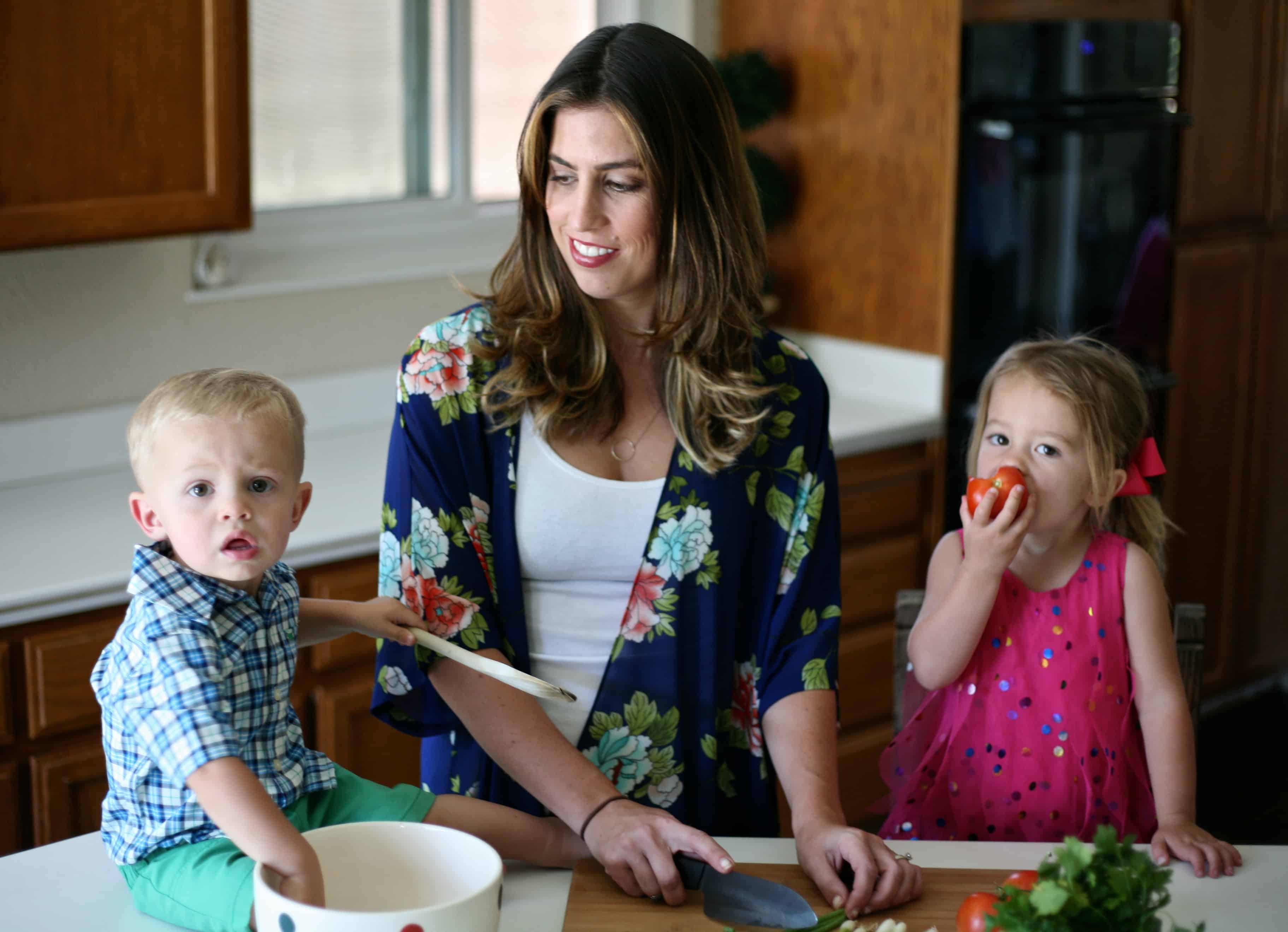 mother with her young son and toddler daughter eating tomatoes and preparing salad on kitchen counter