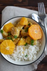 orange chicken on a bed of white rice garnished with fresh orange slices and scallions