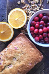 cranberry nut bread next to bowl of cranberries and oranges cut in half