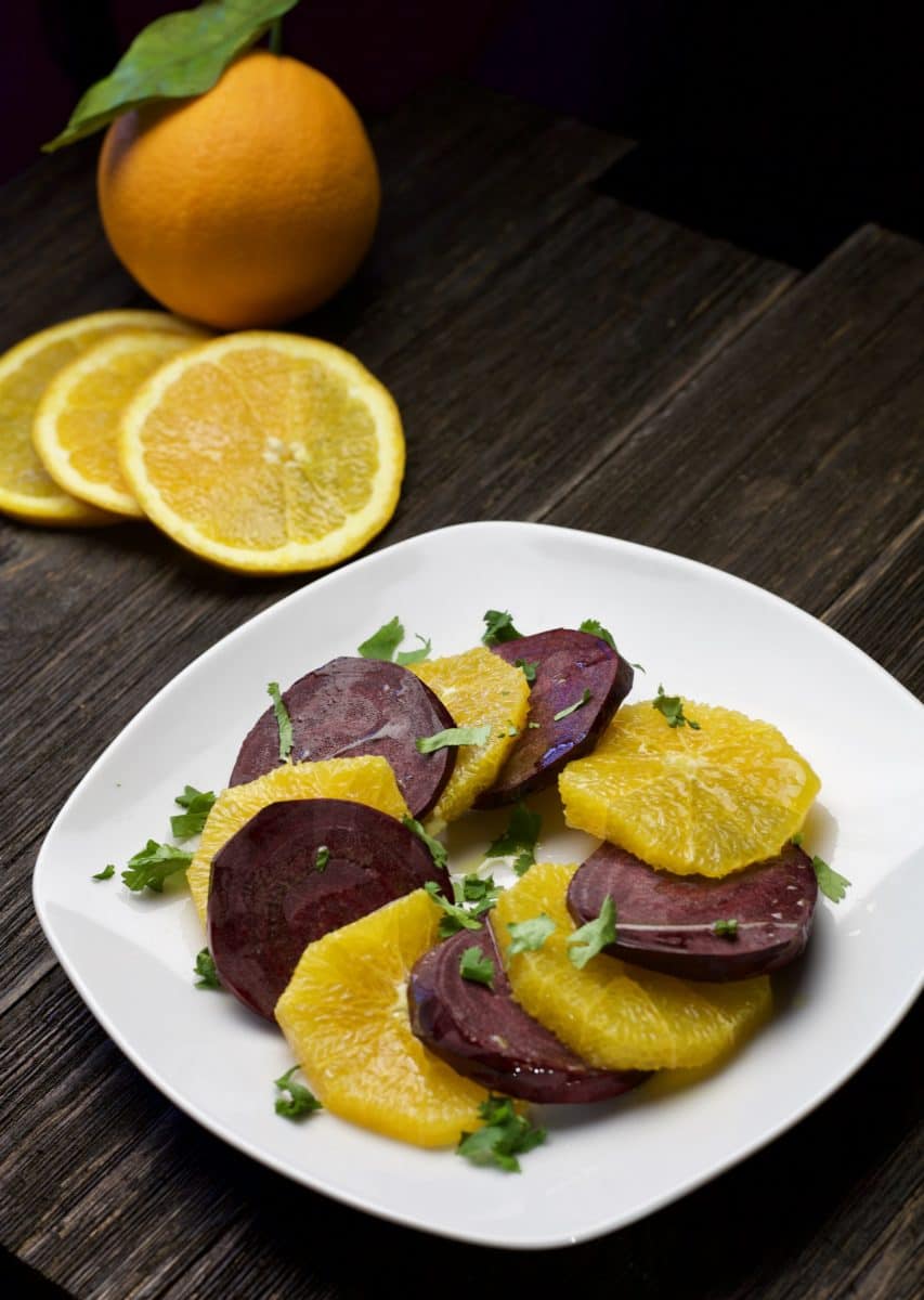 beet and orange salad on white plate with oranges in background