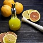 citrus vinaigrette in pour bottle with sliced oranges and juicer surrounding it