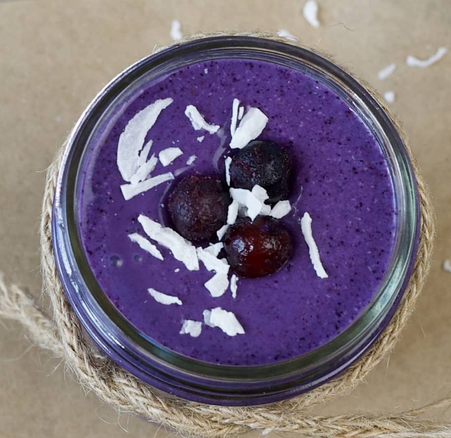 close up of a purple smoothie topped with frozen blueberries and shredded coconut