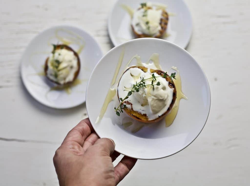 grilled peach half with ice cream, honey and thyme on white plate