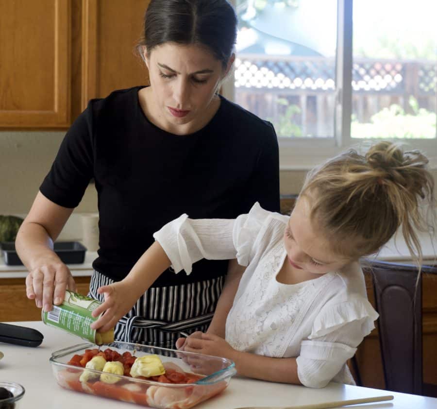 little girl pouring can into pan to bake dinner with mom