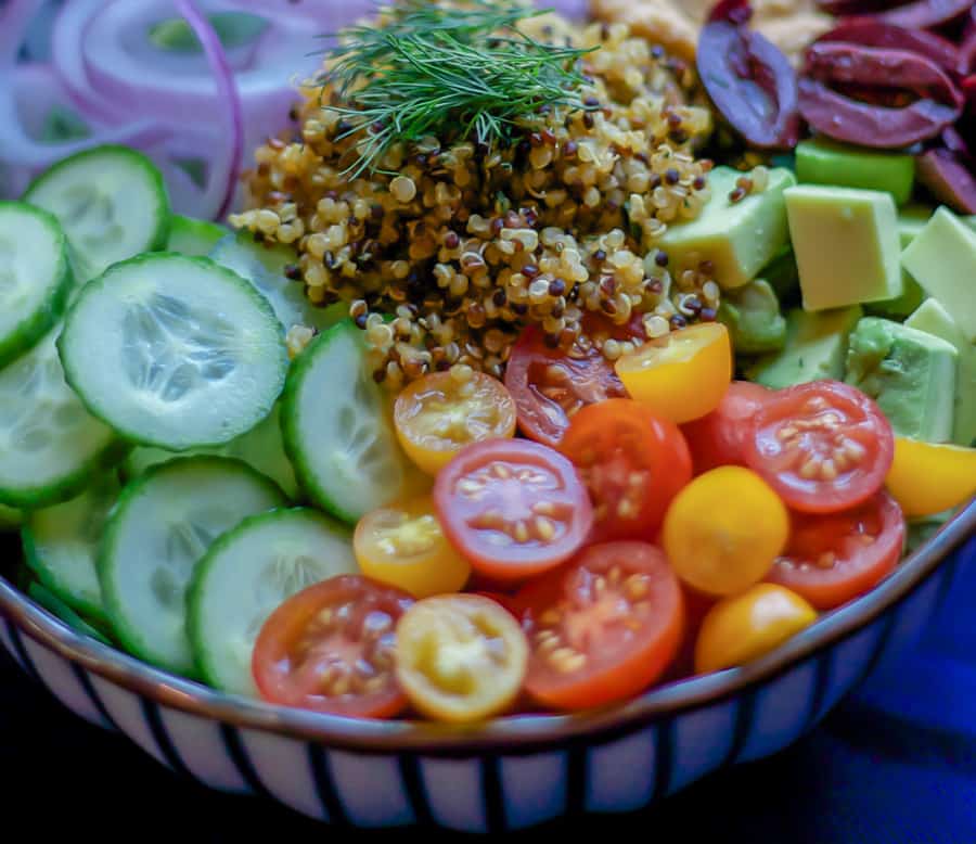 quinoa served on top of cucumbers, olives, hummus, tomato and red onion