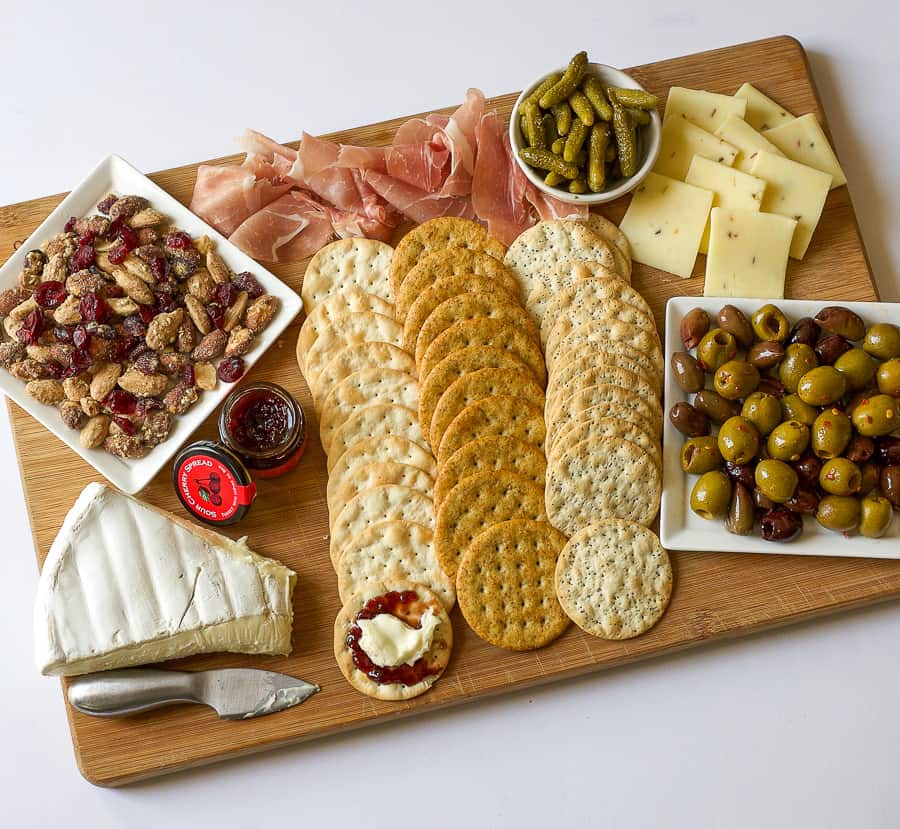 charcuterie board with crackers, cheese, olives, assorted nuts, and mini gherkin