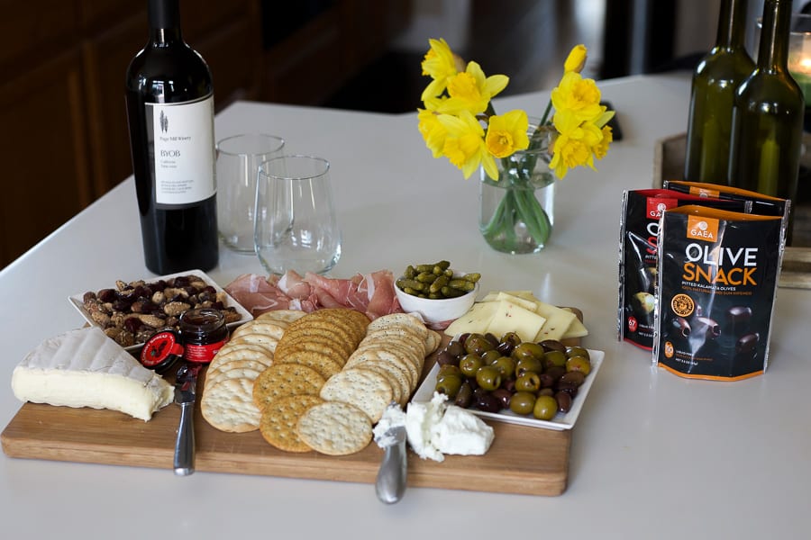 charcuterie board on counter with olives, cheese and wine