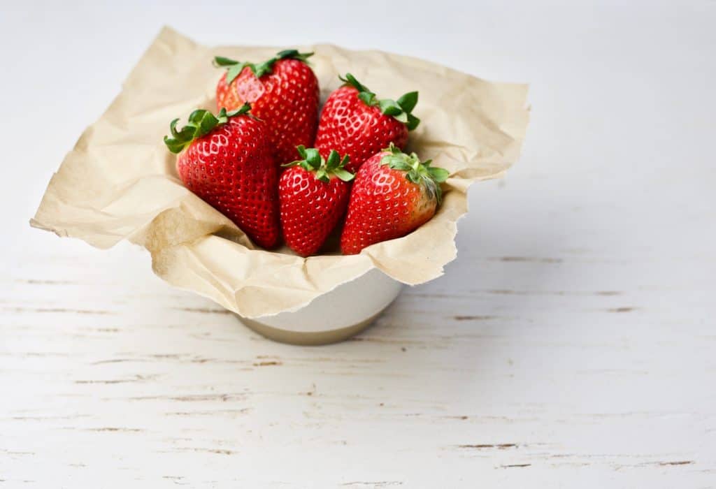 fresh strawberries in white bowl with brown paper