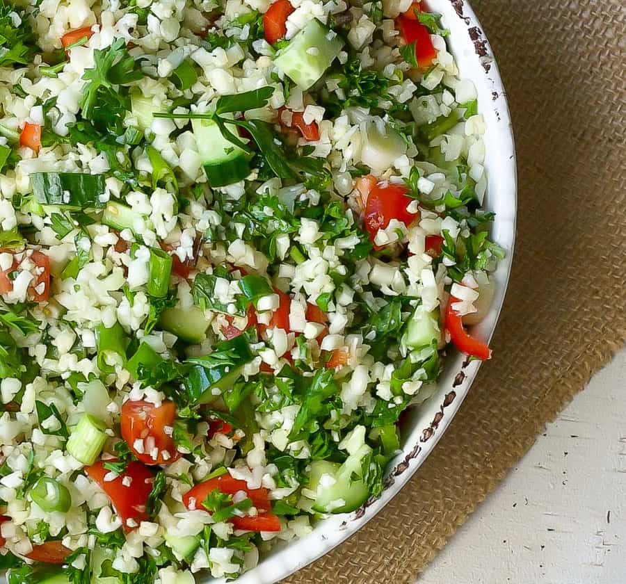 close up bowl of cauliflower rice tabbouleh with fresh herbs cucumber and tomato