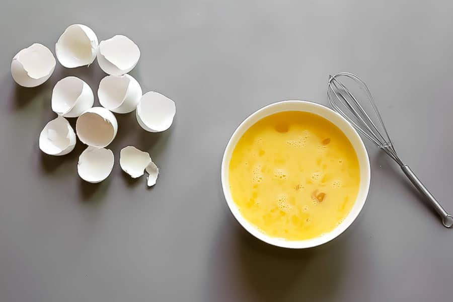 bowl of cracked eggs with shells and whisk