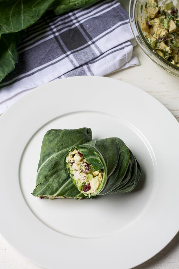 2 halves of a collard green wraps with chicken salad in background