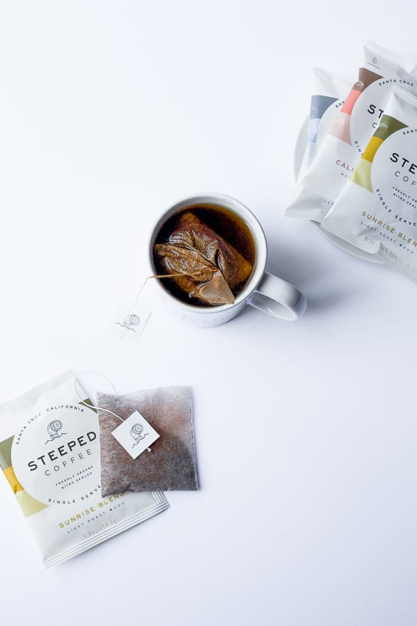 mug of coffee with steeped coffee single serve coffee bags and packaging surrounding