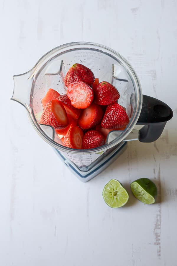 blender with sliced strawberries and lime to make popsicles