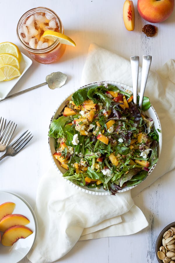 bowl of summer peach salad with couscous and pistachios with iced tea and sliced peaches surrounding